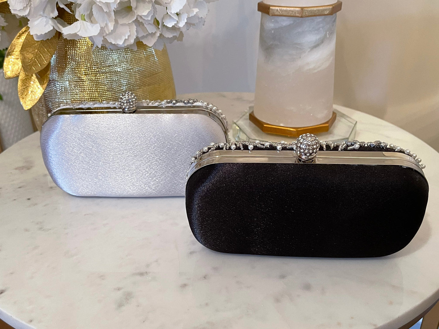 Here’s a specific SEO alt tag for the product in the silver and black variations showcasing the plain back of the bags against a marble and gold background:
Silver and black clutch bags displayed from the back on a marble and gold background, highlighting their simple, elegant design