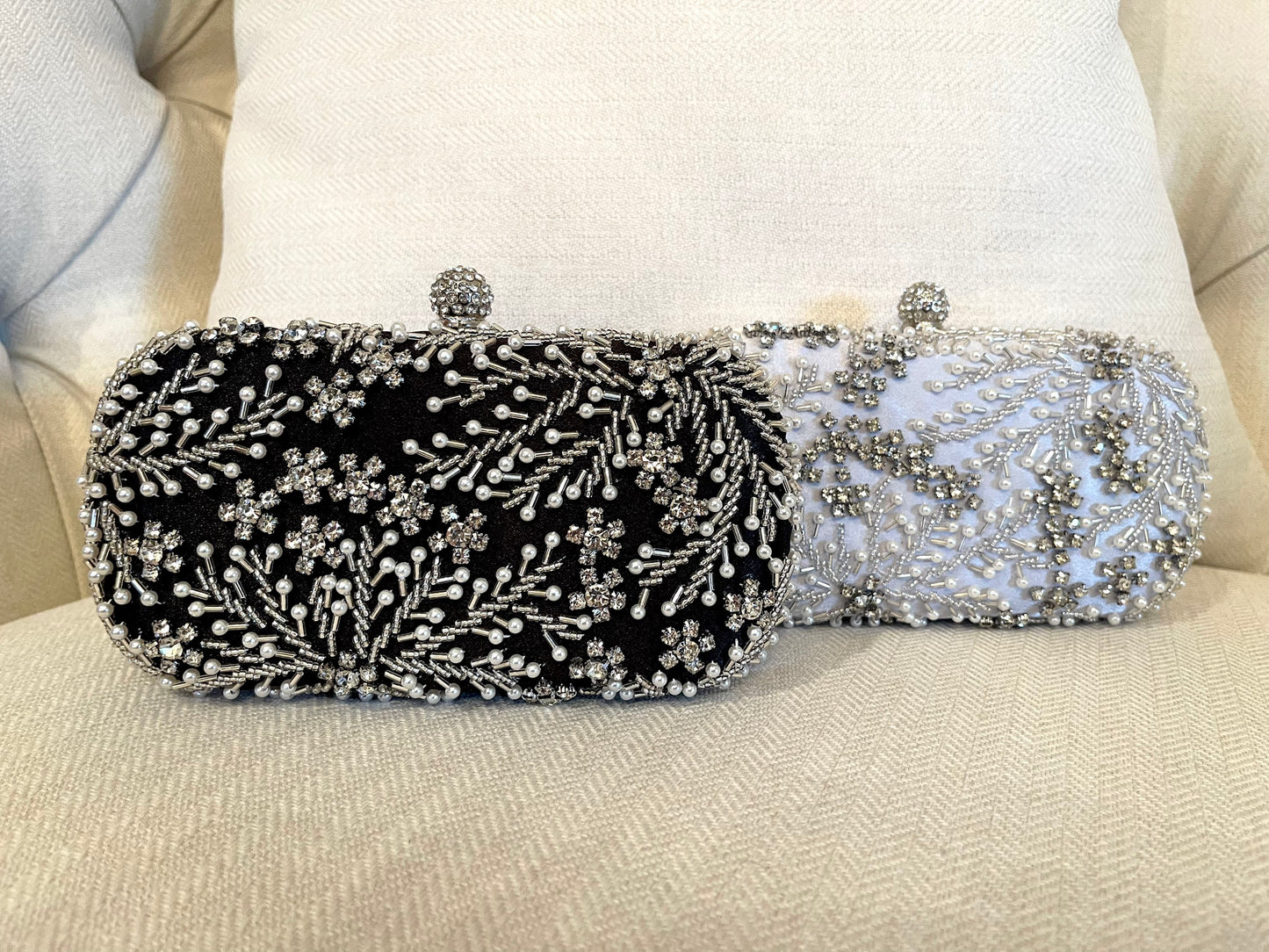 Front view of both the silver and black crystal leaves and pearl beads embroidered clutch with gold and white details in the background