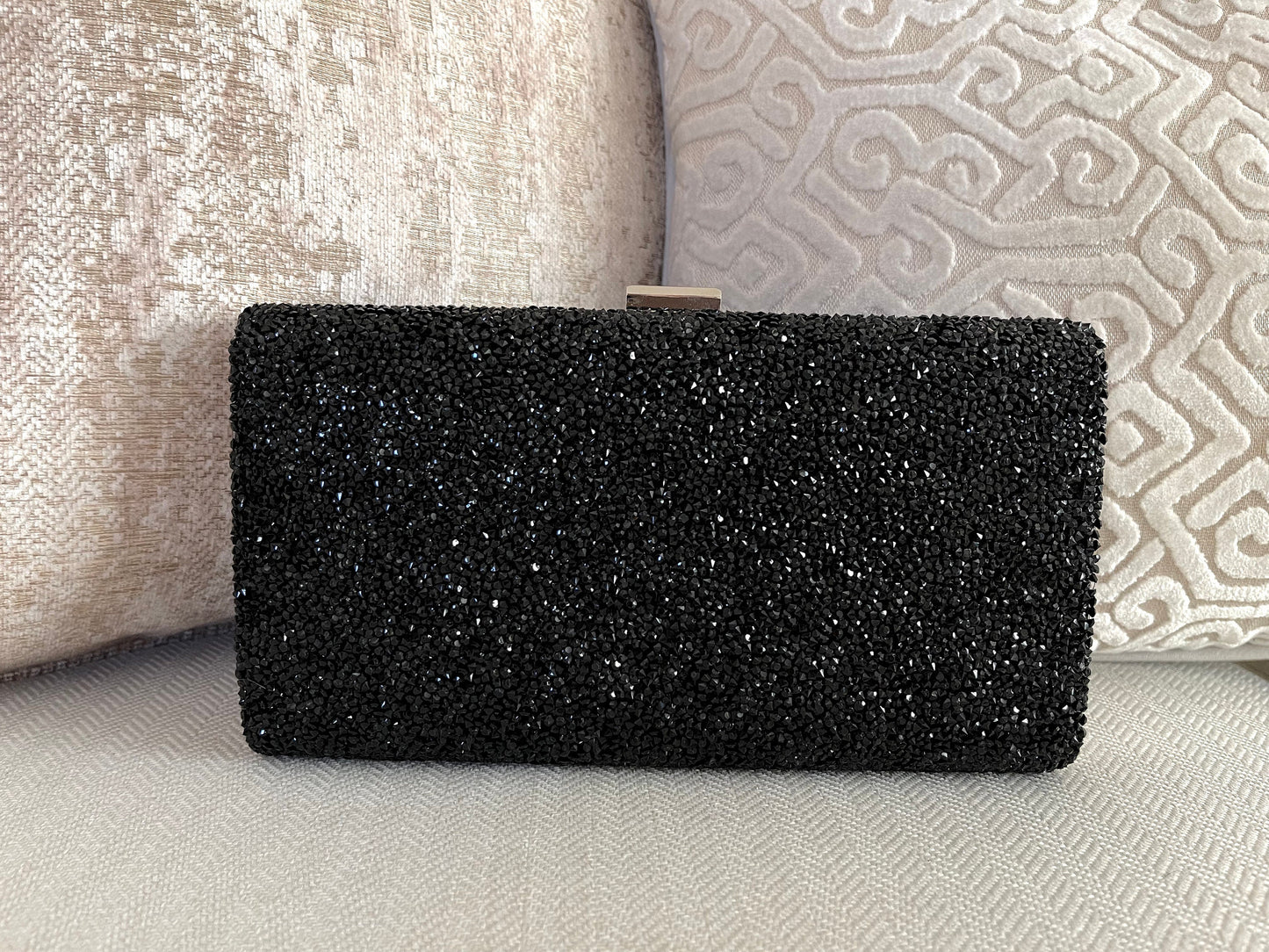 Black shimmer clutch purse showcasing front design against a neutral design background