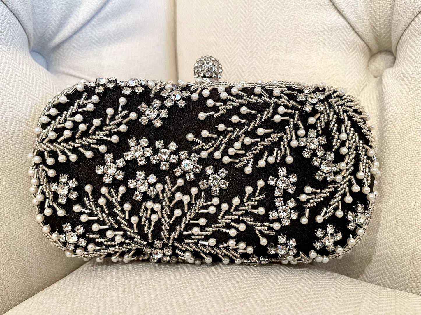 Front view of black crystal leaves and pearl beads embroidered clutch with a neutral background. 