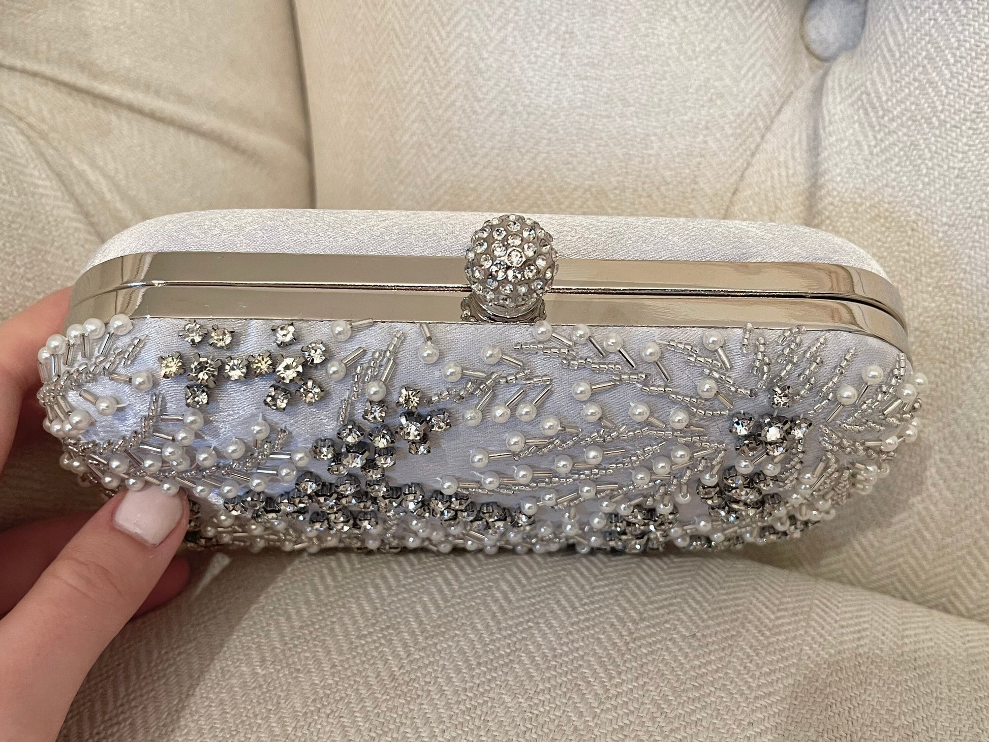 Top-down view of silver clutch highlighting the bedazzled clasp detail against a neutral background.