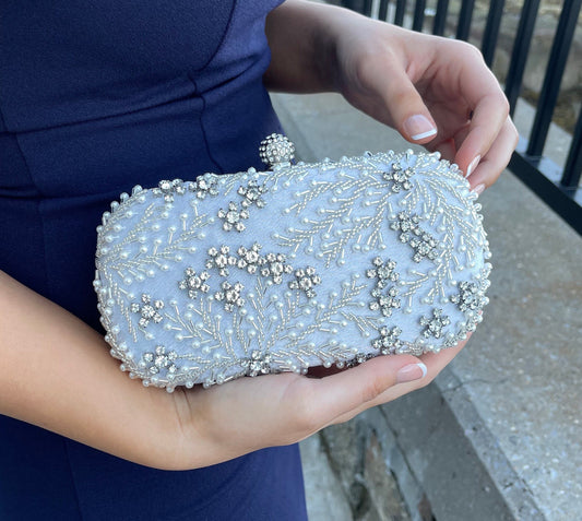 Silver crystal leaves and pearl beads embroidered clutch held against a blue dress