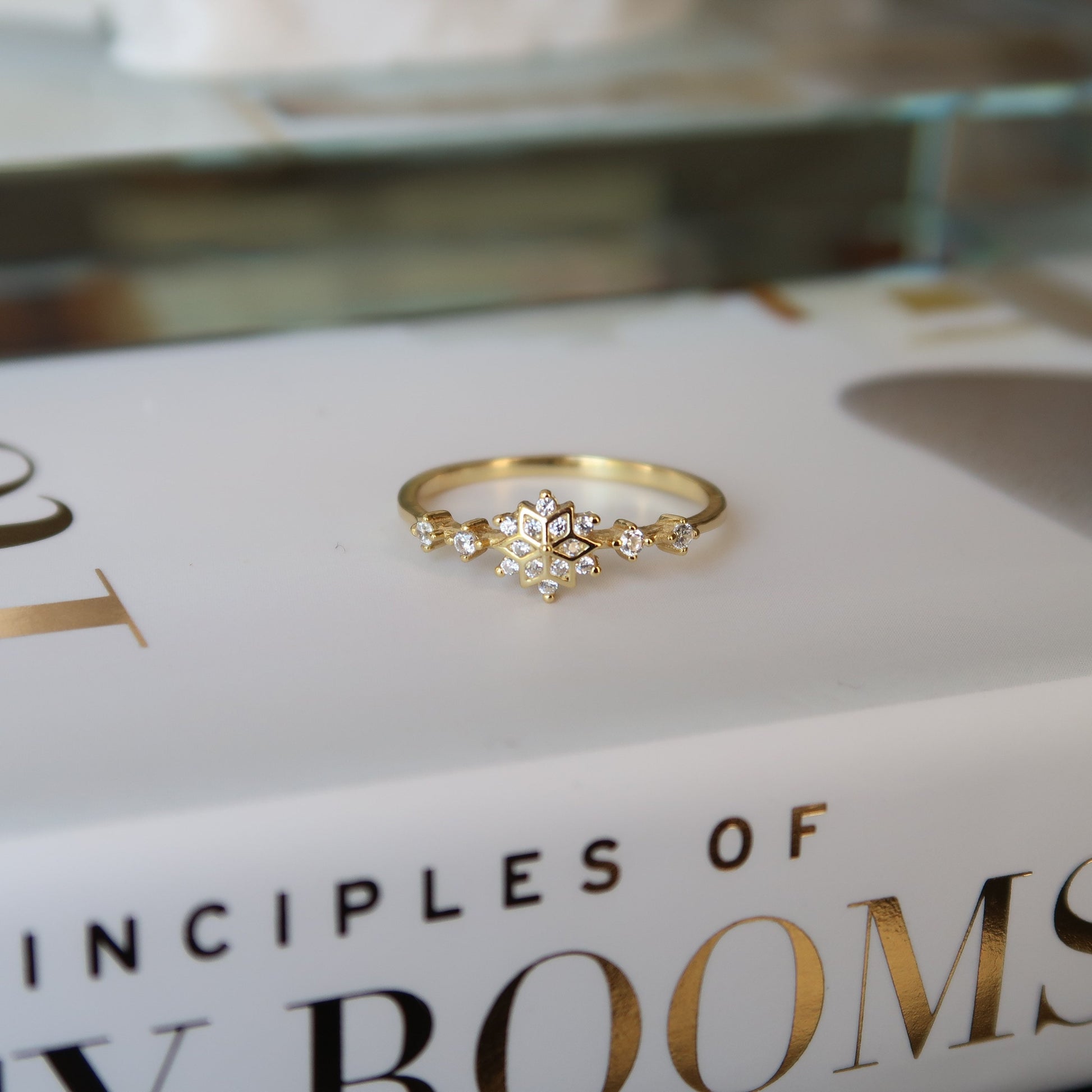 Gold snowflake ring modeled on top of a decorative book, emphasizing its minimalist elegance and cubic zirconia sparkle.