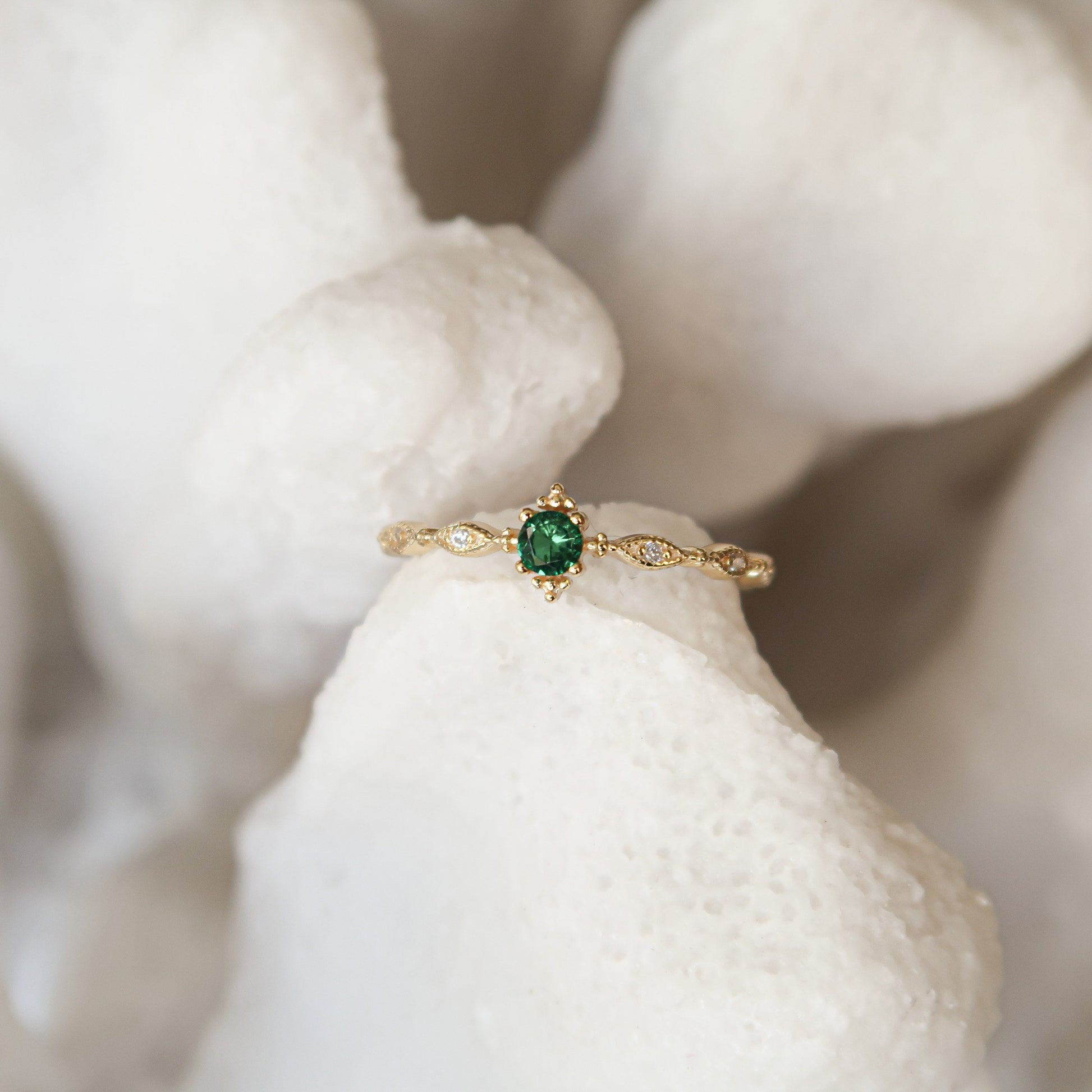 Faux Emerald Dainty Ring positioned against a fake white coral decoration, emphasizing its delicate and colorful design.