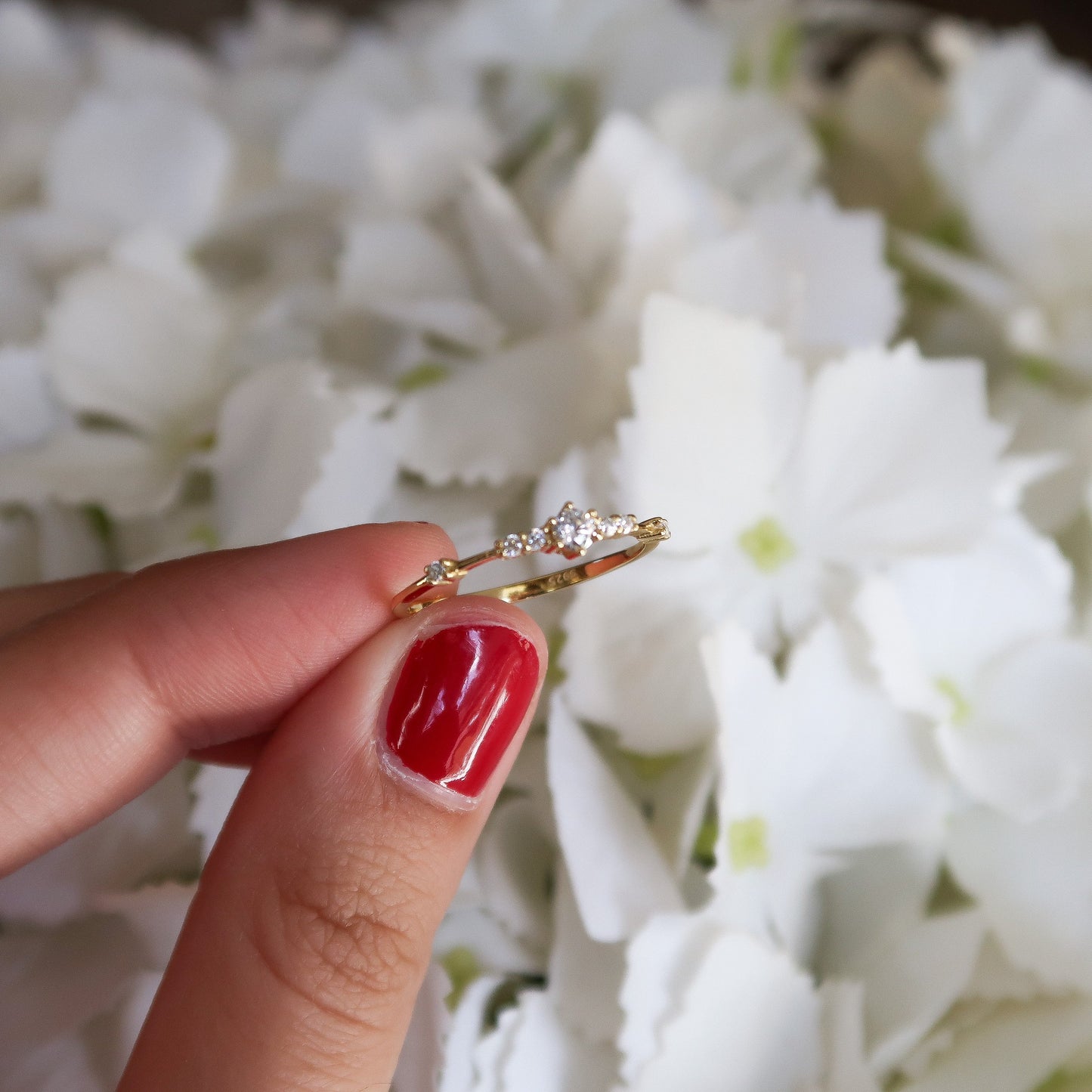 Gold cubic zirconia ring held up against a white floral background, showcasing its elegant, minimalist style and sparkling stone.