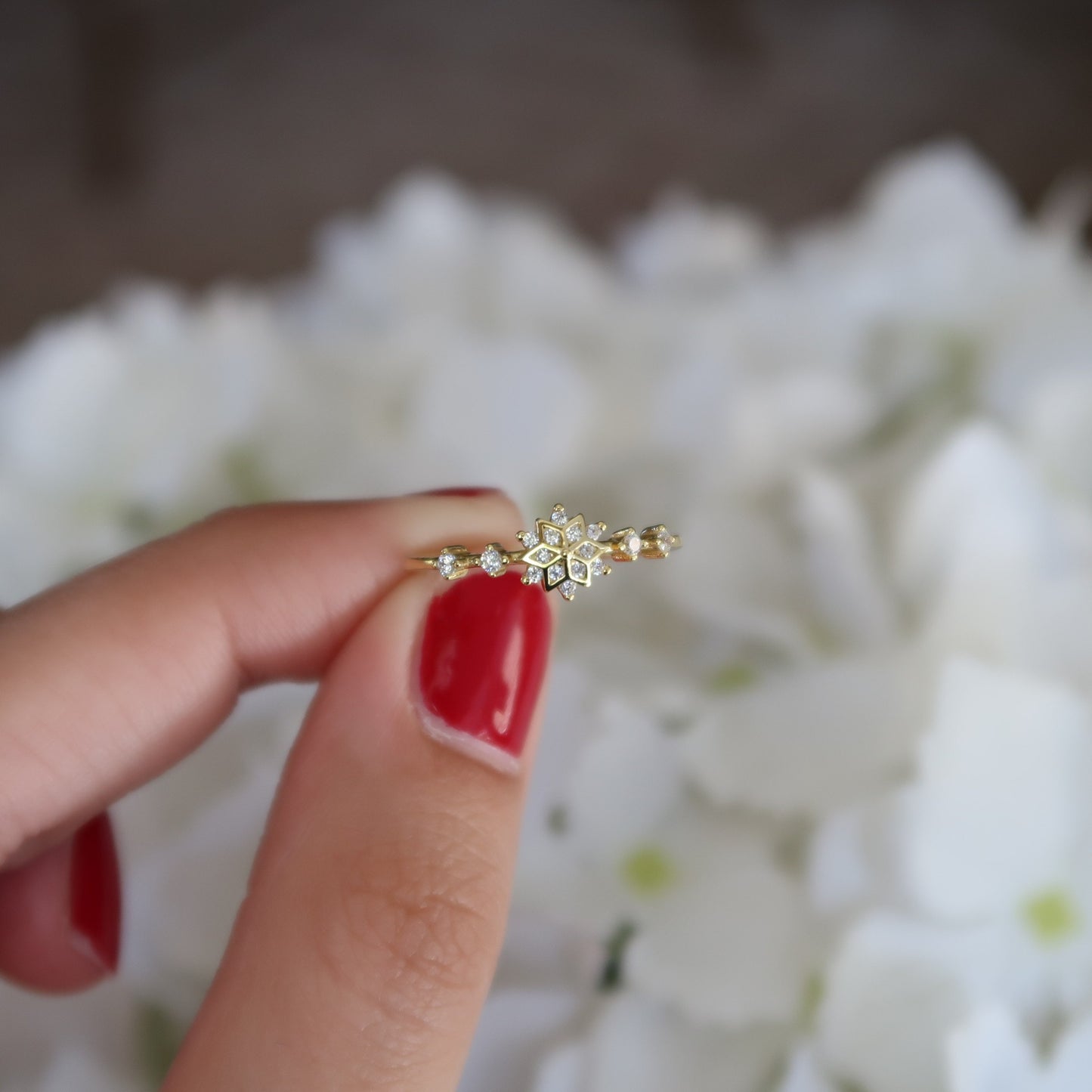 Gold snowflake ring held up against a white floral background, highlighting its minimalist design with sparkling cubic zirconia stones