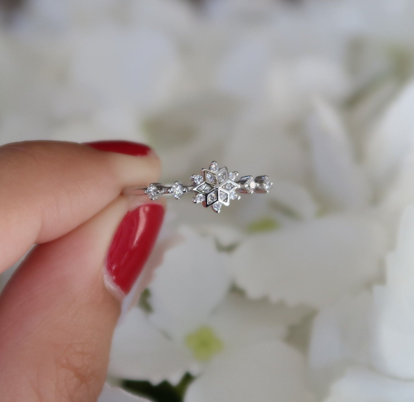 Silver snowflake ring held up against a white floral background, showcasing its dainty design and cubic zirconia accents.