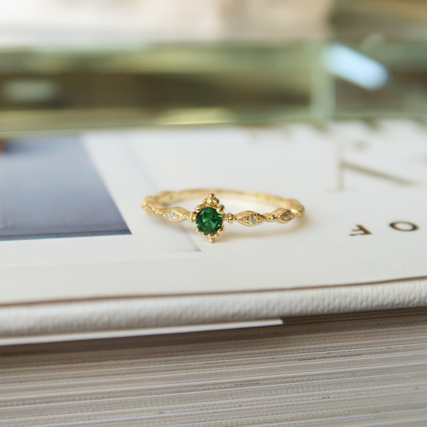 Faux Emerald Dainty Ring displayed on a book, showcasing its elegant design and cubic zirconia stones