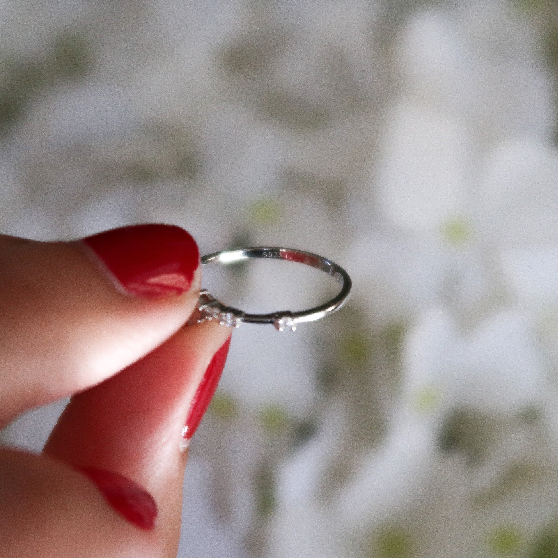 Silver cubic zirconia ring held up against a white floral background, featuring a delicate, dainty design with brilliant sparkle.