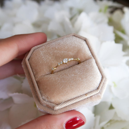 Gold cubic zirconia ring modeled in a beige ring case against a white floral background, highlighting its dainty, minimalist design.