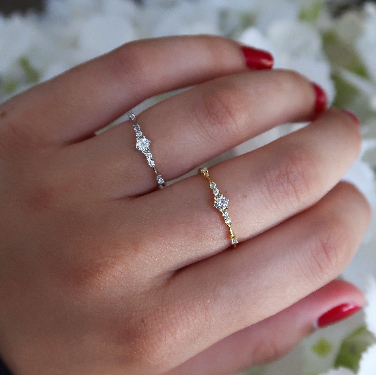 Gold and silver cubic zirconia rings modeled on a hand, demonstrating their minimalist and stackable style against a white floral background.