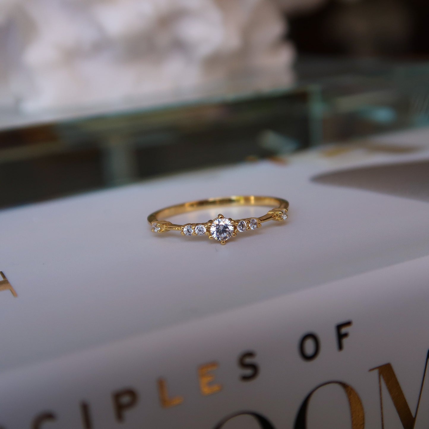 Gold cubic zirconia ring modeled flat against a decorative book, emphasizing its subtle elegance and minimalist design.