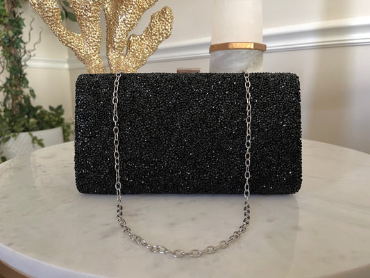 Black shimmer clutch purse showcasing front design and silver chain on a marble table