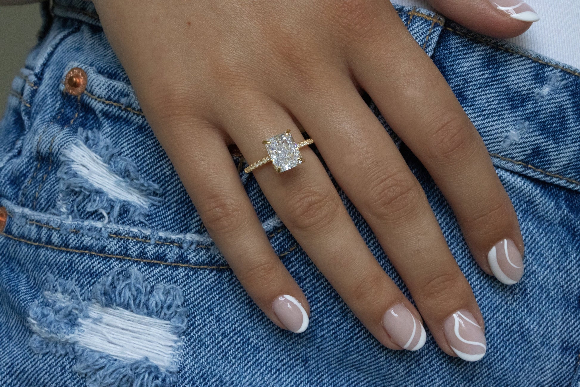 Radiant Cut Engagement Ring displayed on a ring finger, contrasting beautifully against denim jeans.