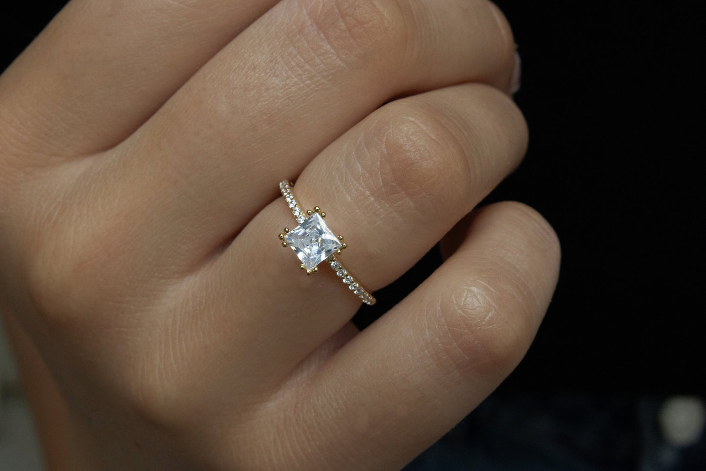 Close-up of Princess Cut Ring modeled on a hand against a dark background, showcasing the gold finish and cubic zirconia stones.