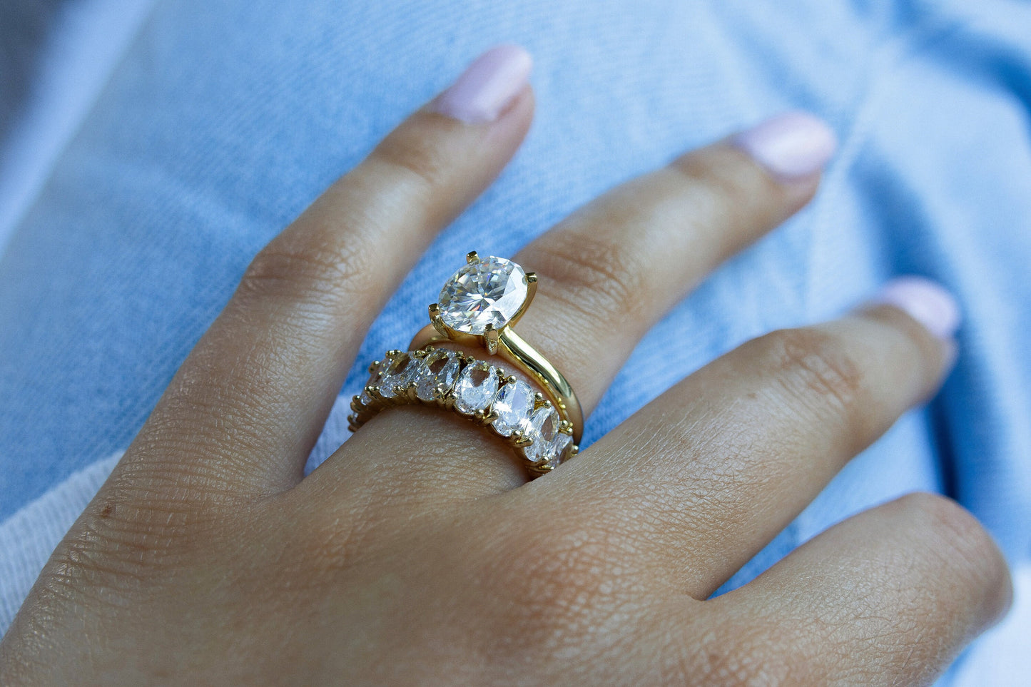 Model showcasing 3CT Oval Moissanite Engagement Ring in Yellow Gold stacked with another ring from a downward angle showcasing the setting of the ring