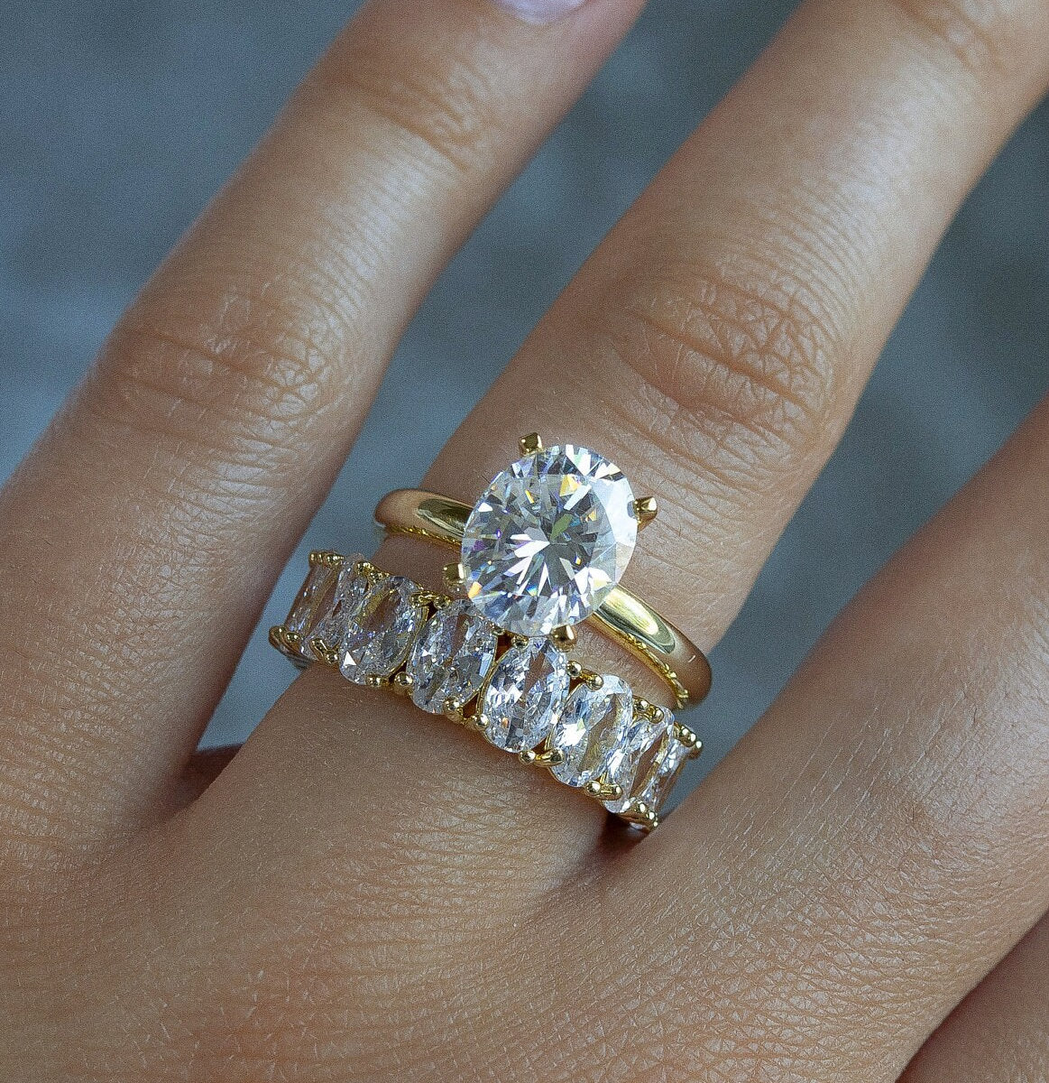 Model showcasing 3CT Oval Moissanite Engagement Ring in Yellow Gold stacked with another ring