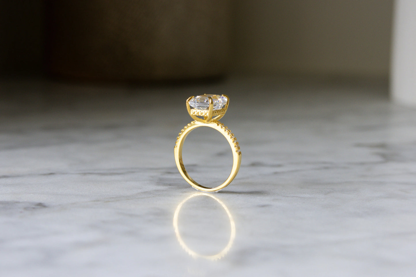 Side view of the gold Radiant Cut Engagement Ring on a marble background, emphasizing its sleek profile and exquisite craftsmanship.