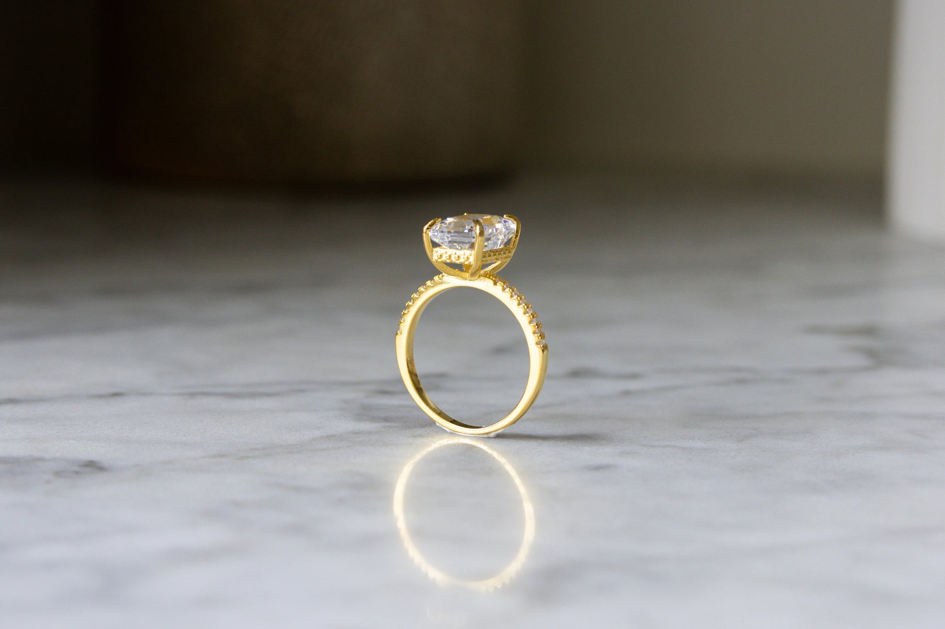 Side view of the gold Radiant Cut Engagement Ring on a marble background, emphasizing its sleek profile and exquisite craftsmanship.