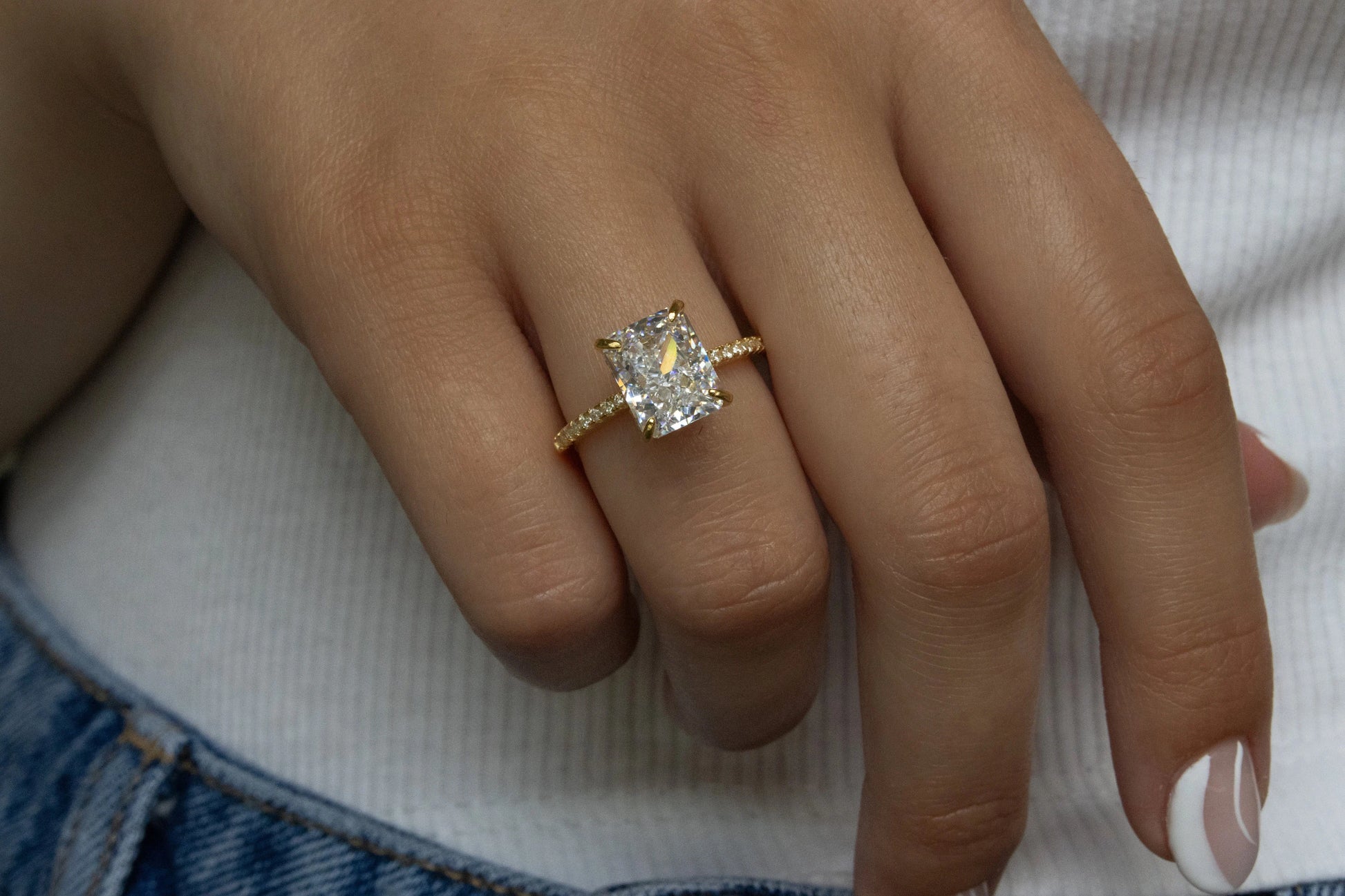 Gold Radiant Cut Engagement Ring showcased on the ring finger of a model against a white t-shirt background, highlighting its elegance.