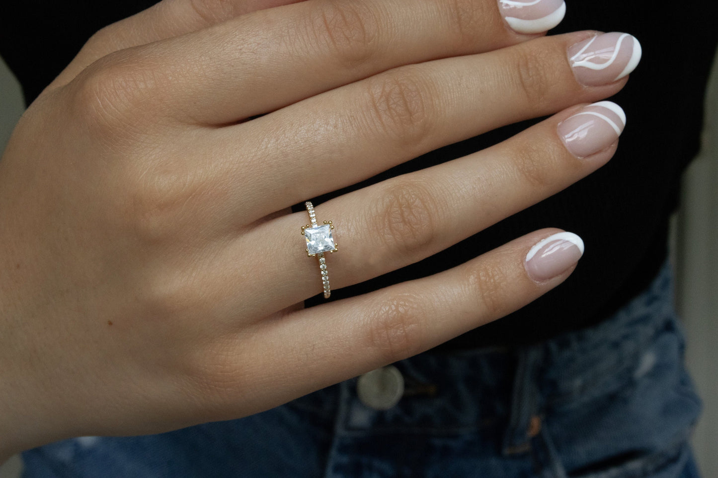 Model wearing Princess Cut Ring on a hand, with a dark background to enhance the contrast and gold tone.