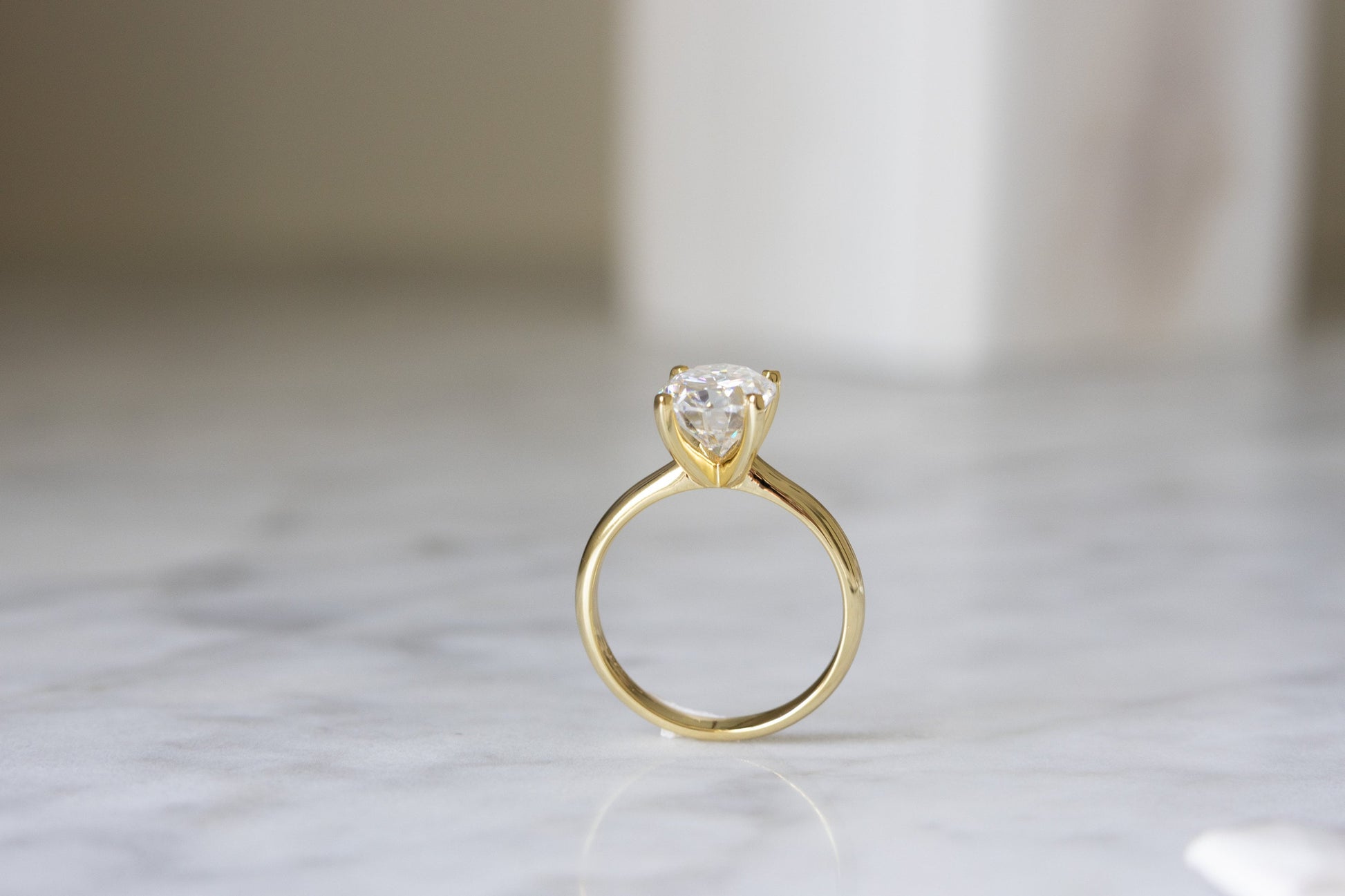 3CT Oval Moissanite Engagement Ring in Yellow Gold standing up against a marble background