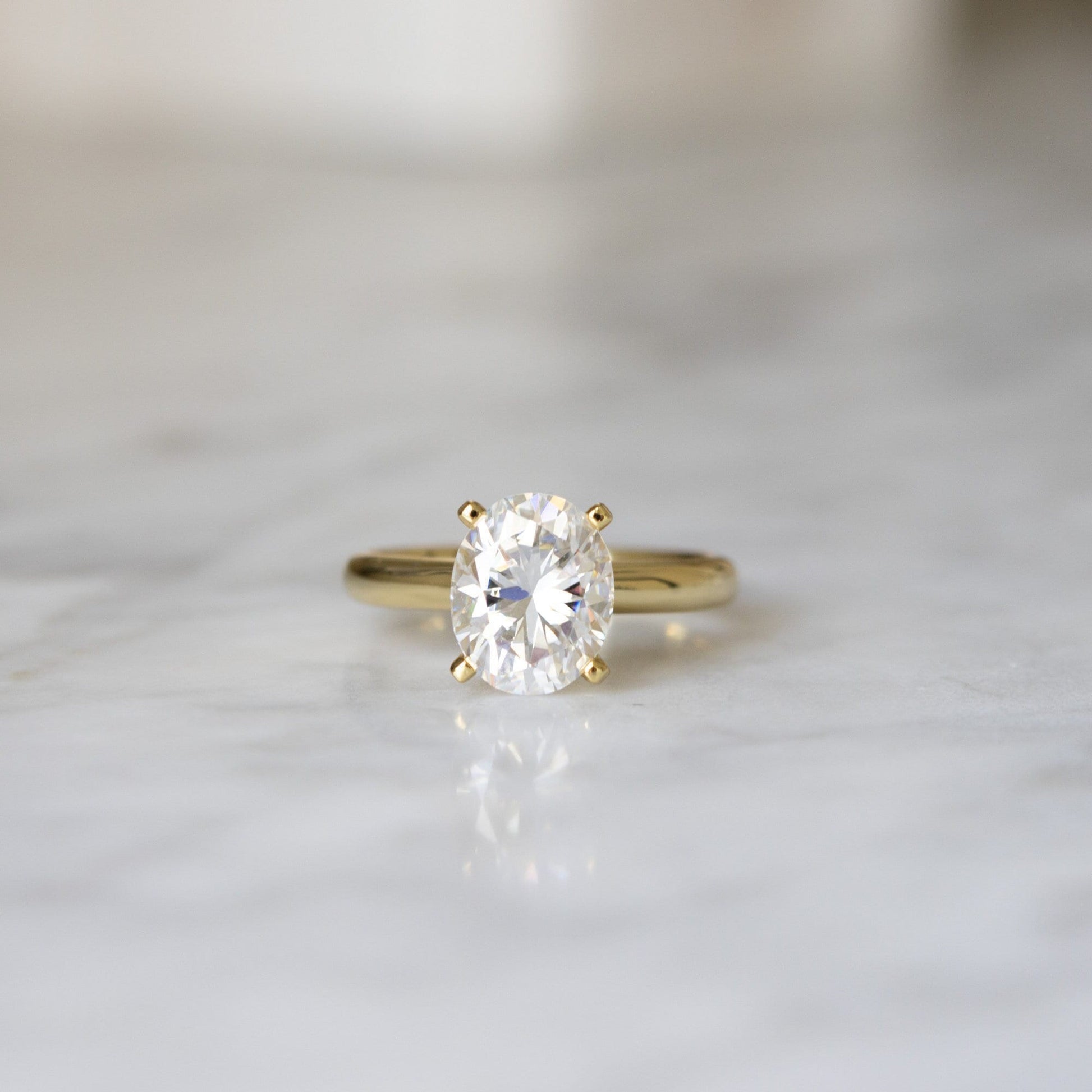 Close-up of 3CT Oval Moissanite Stone on Engagement Ring against a marble background