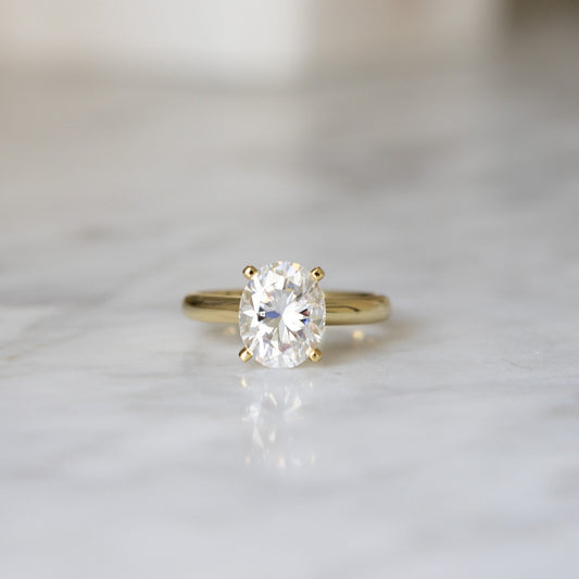 Close-up of 3CT Oval Moissanite Stone on Engagement Ring against a marble background