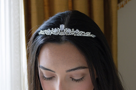 Model with dark hair showcasing a stunning crystal wedding tiara against a luxurious gold background.