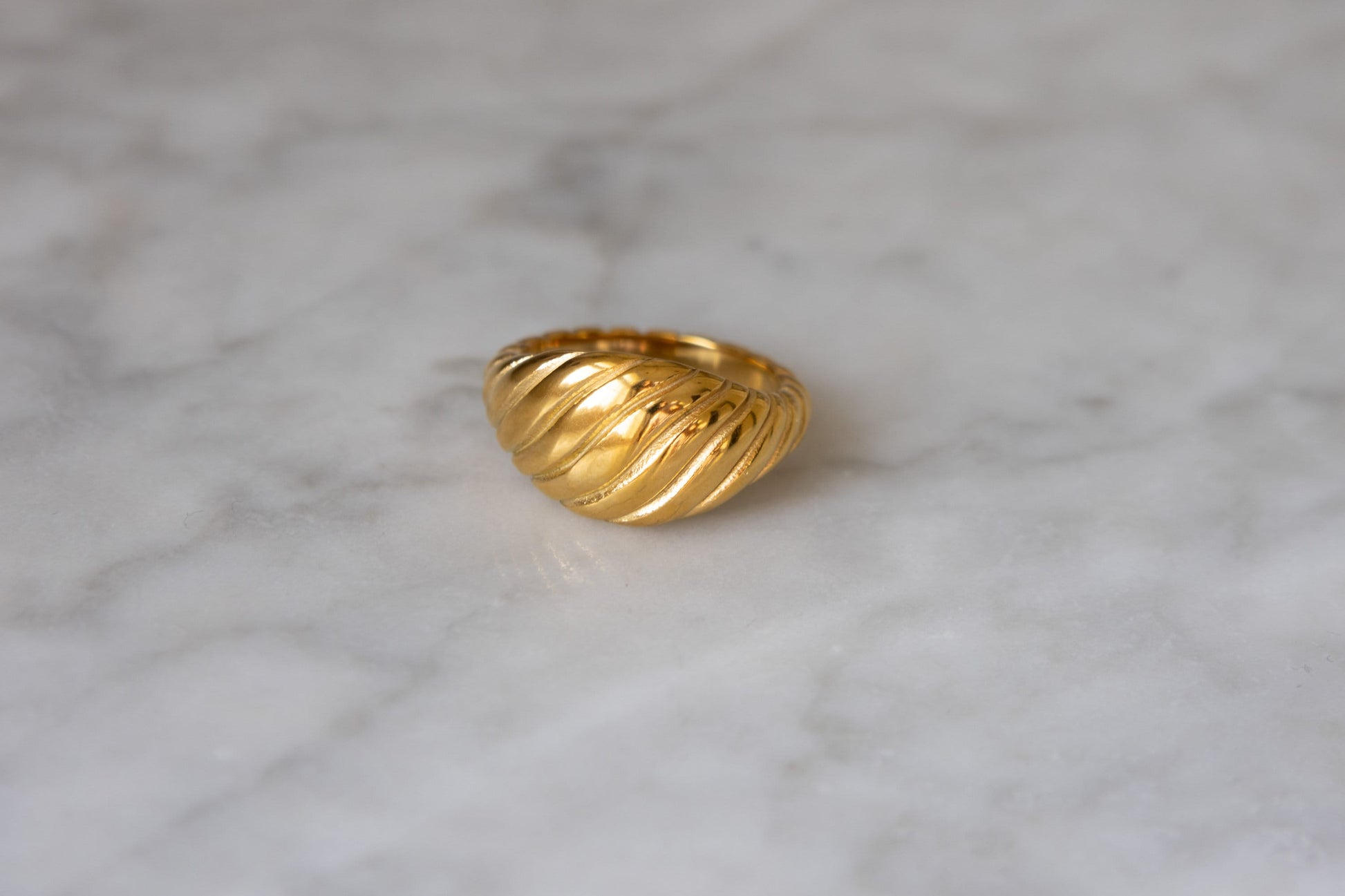 Twisted 18k gold croissant ring on marble background from a top angle