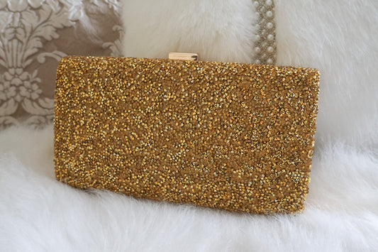 Gold shimmer clutch purse against a white fluffy background, perfect for evening events and weddings