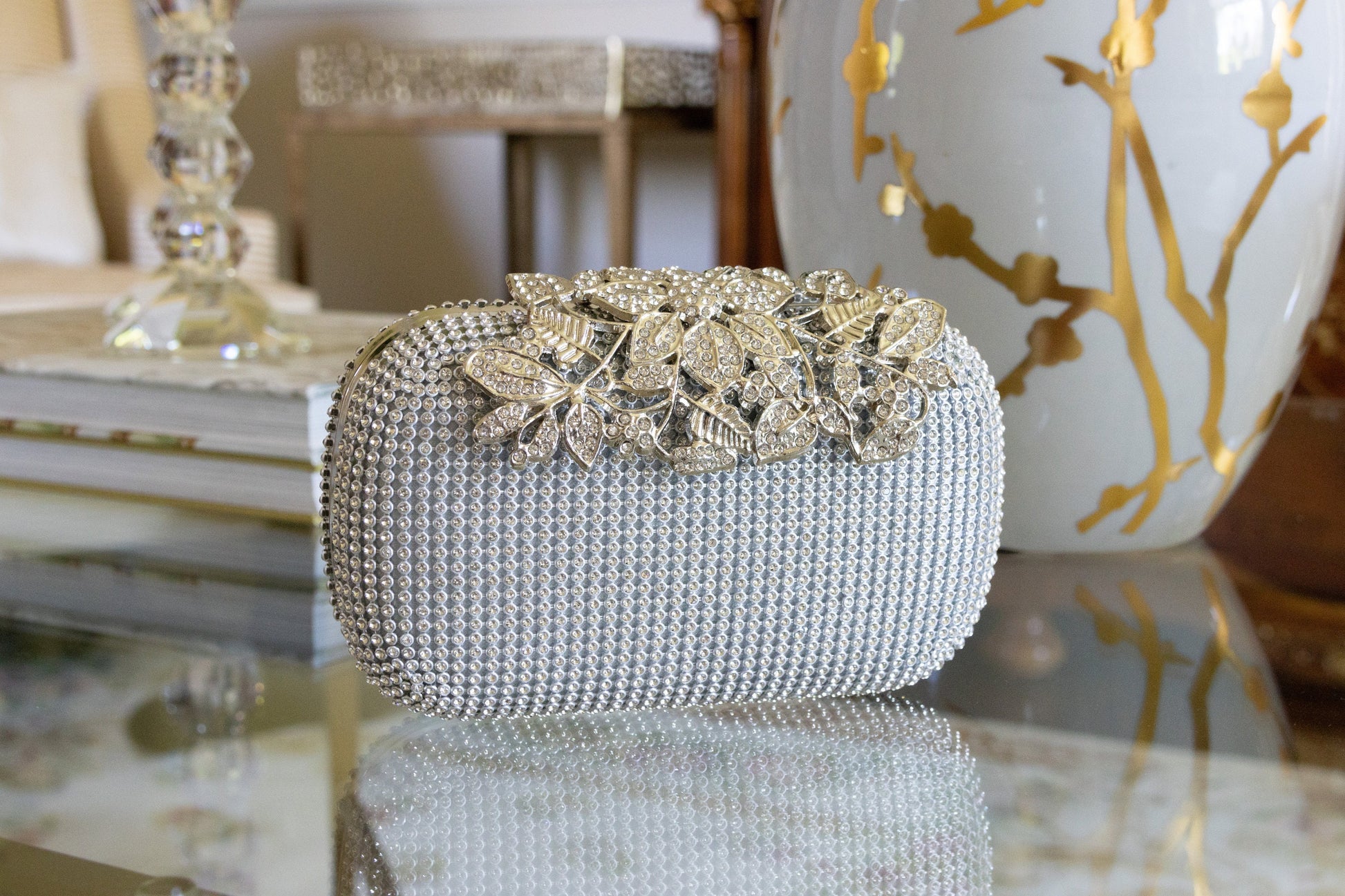 Front view of a silver crystal purse against a white and gold background, highlighting the bedazzled design and elegant finish.