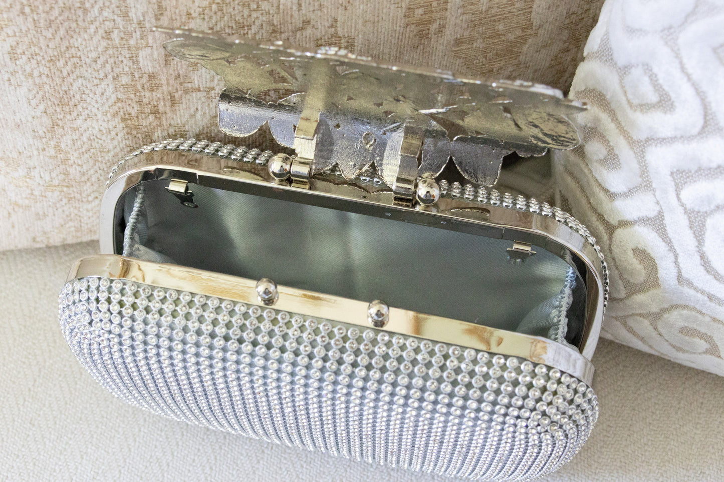 Interior view of a silver crystal purse against a white and gold background, highlighting the bedazzled design and elegant finish.