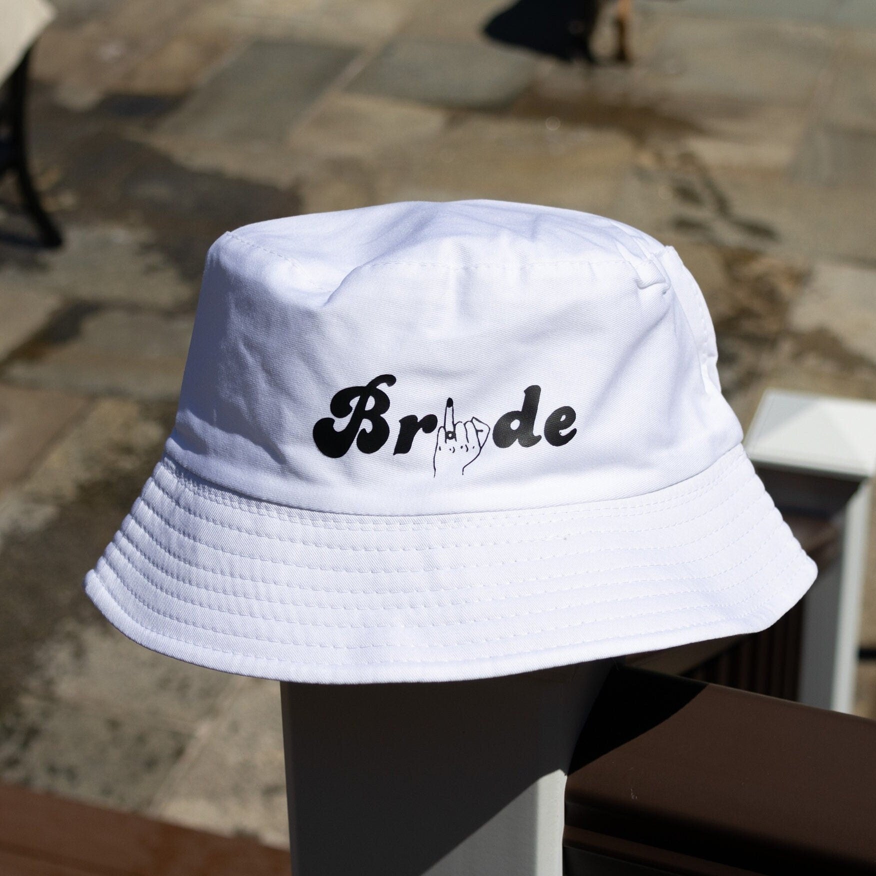 Front view of a bride bucket hat, modeled with bridal text in a fun font against a brown background