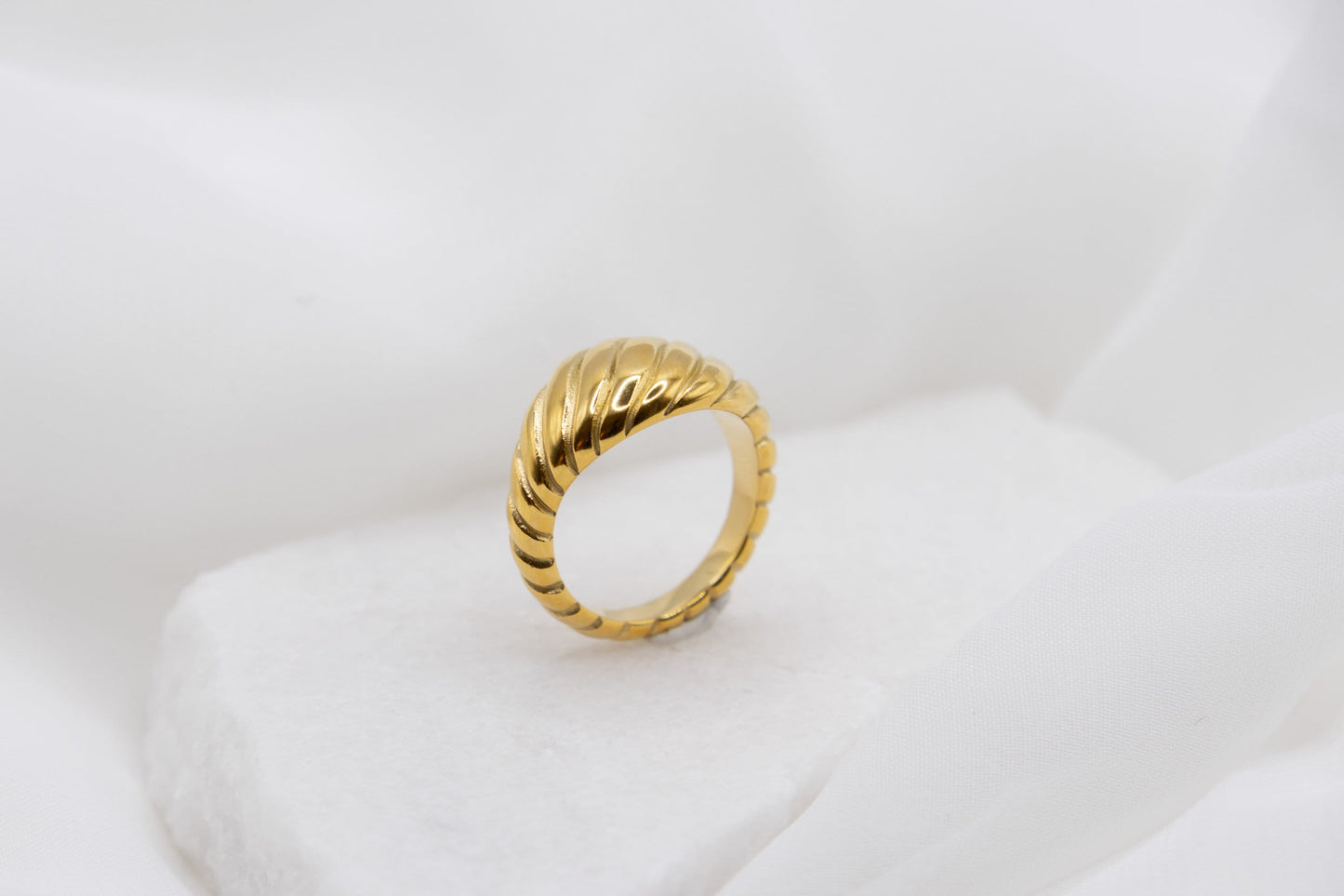 Twisted gold croissant ring standing pu against a white background