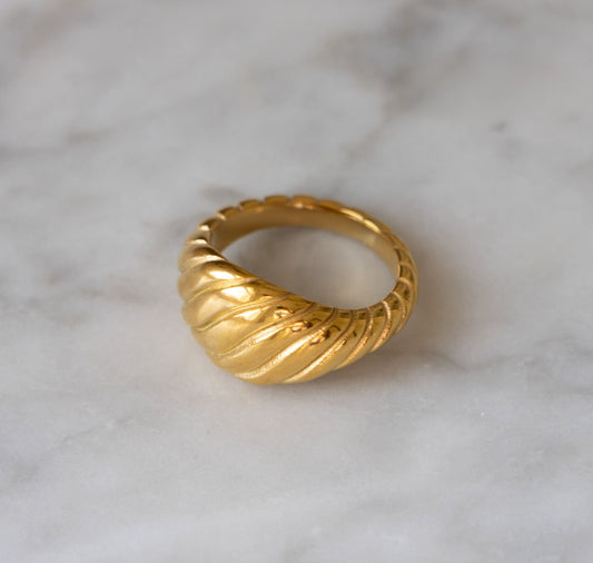 Twisted gold croissant ring on marble background from a top angle