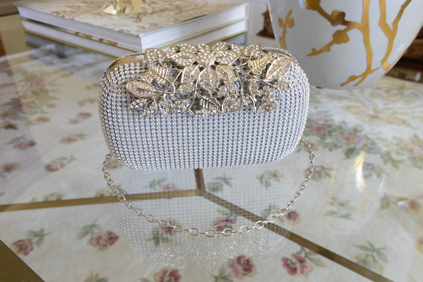 Front view of a silver crystal purse against a white and gold background, highlighting the bedazzled design and elegant finish, showcasing the removable chain option. 