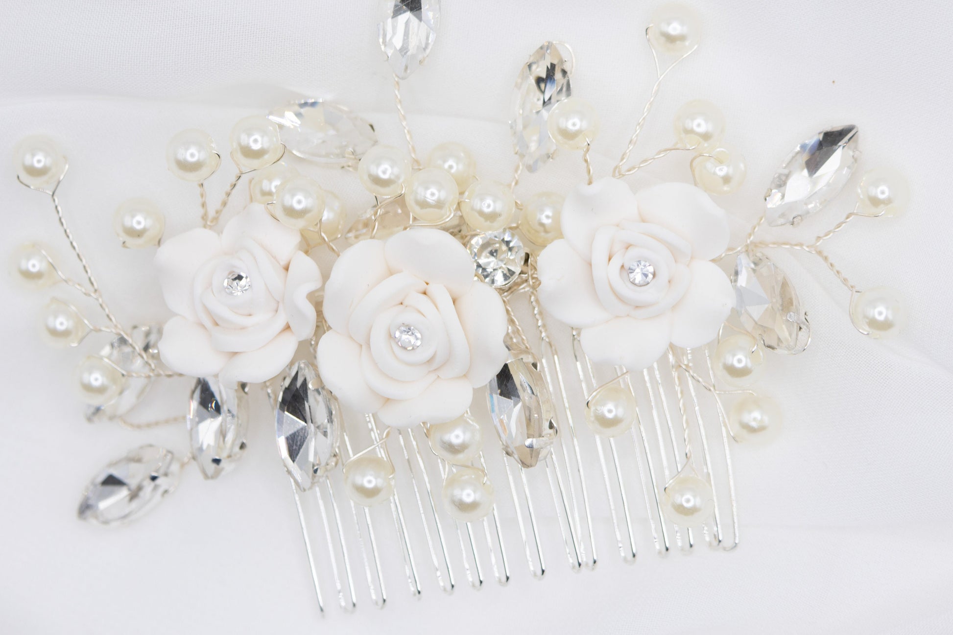 Close-up of a silver wedding hair pin featuring flower design, rhinestones, and faux pearls on a white background